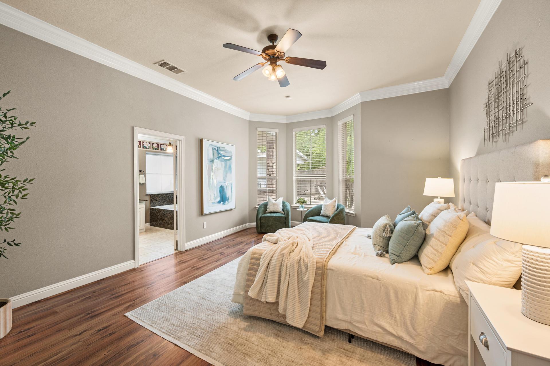 Primary bedroom with wood-look flooring, ceiling fan, and doorway to the ensuite bathroom and closet