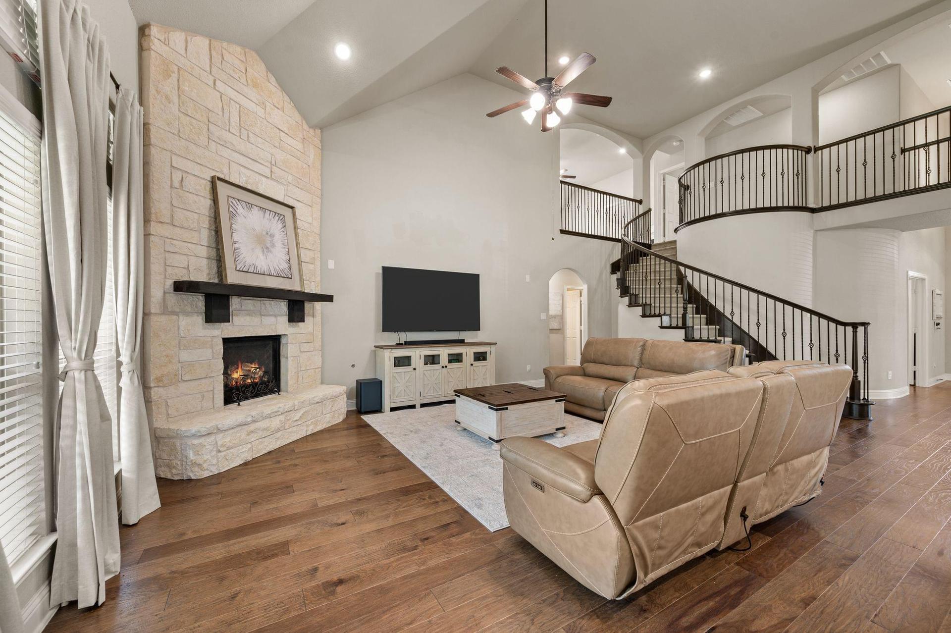 Open-concept living room at 4201 Rainwater Creek Way in Celina, TX, featuring a stone fireplace, soaring ceilings, hardwood floors, and curved staircase.