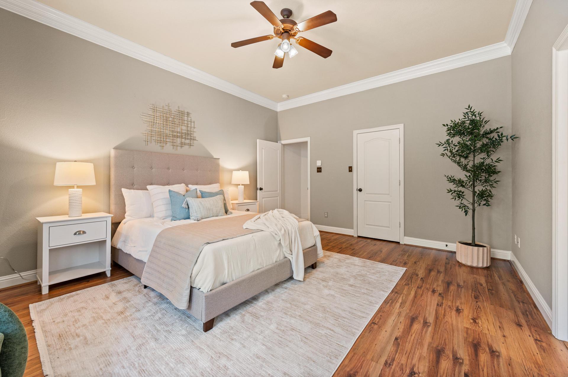 Bedroom with wood-look flooring, ceiling fan, large windows, and adjoining bathroom entrance