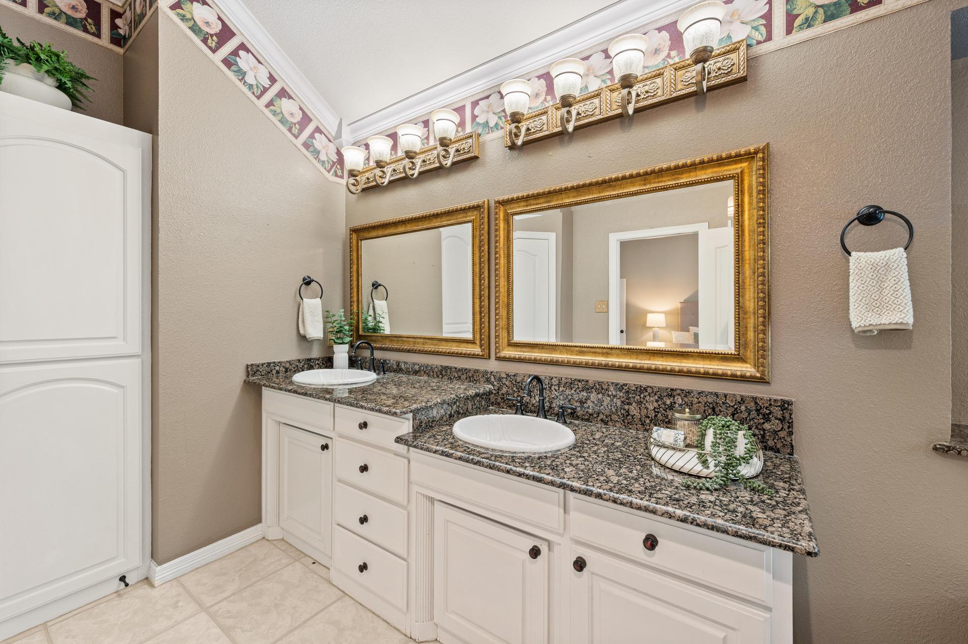Bathroom with double-sink vanity, dark granite countertops, white cabinetry, and tub-shower combination
