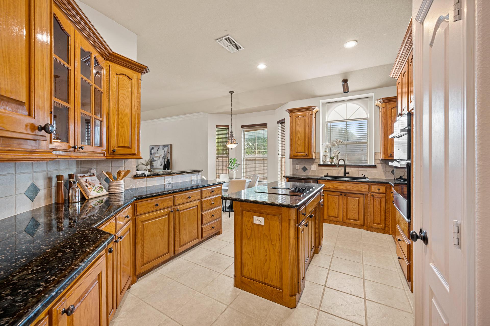 Kitchen with wood cabinetry, granite countertops, tile flooring, and a central island